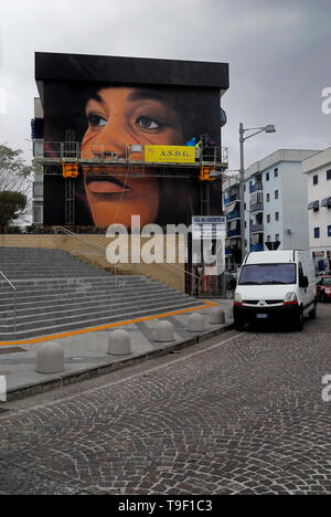 Agoch Jorit, 28, rue napolitaine est artiste de renommée internationale, père et mère néerlandaise. Il crée des peintures murales géantes sur les façades des immeubles de banlieue à travers le monde. Ses œuvres sont présentes à Buenos Aires, Córdoba, Aruba, Santiago du Chili, New York, Miami, Las Vegas, Los Angeles, San Francisco, Shenzhen, Gaza. En Italie Jorit est principalement actif à Naples où il fait d'immenses peintures sur façades aveugles des immeubles de banlieue et aussi dans le centre historique. Banlieue de Naples, bâtiments populaires de mauvaise réputation de Scampia trimestre. La peinture de Angela Davis. Banque D'Images