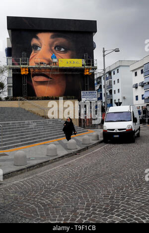 Agoch Jorit, 28, rue napolitaine est artiste de renommée internationale, père et mère néerlandaise. Il crée des peintures murales géantes sur les façades des immeubles de banlieue à travers le monde. Ses œuvres sont présentes à Buenos Aires, Córdoba, Aruba, Santiago du Chili, New York, Miami, Las Vegas, Los Angeles, San Francisco, Shenzhen, Gaza. En Italie Jorit est principalement actif à Naples où il fait d'immenses peintures sur façades aveugles des immeubles de banlieue et aussi dans le centre historique. Banlieue de Naples, bâtiments populaires de mauvaise réputation de Scampia trimestre. La peinture de Angela Davis. Banque D'Images