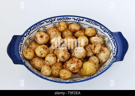 Les jeunes pommes de terre pelées dans les épices préparé pour la cuisson dans une forme en céramique sur un fond blanc, vue du dessus Banque D'Images