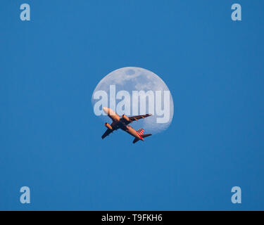 Un avion passe devant la lune au coucher du soleil peu après le décollage. Banque D'Images