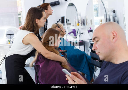 Teen girl recevoir dans ce type de coiffure professionnel alors que son père, absorbé dans le téléphone Banque D'Images