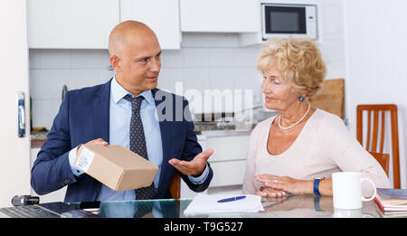 Représentant des ventes passant de carton avec des marchandises commandées à femme âgée dans la cuisine Banque D'Images