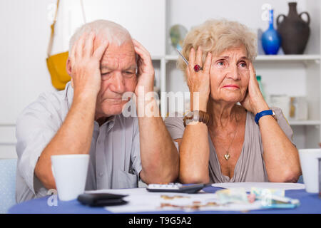 Couple frustrés face à des ennuis financiers table avec titres, espèces et calculatrice Banque D'Images