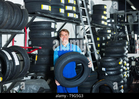 Portrait of smiling mature man mécanicien dans une combinaison protectrice avec pneus auto en atelier Banque D'Images