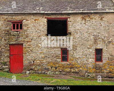 Vieilles pierres couvertes de lichens grange avec toiture en ardoise et fatigué de la peinture rouge sur les boiseries irrégulières en Cumbria, Angleterre, Royaume-Uni Banque D'Images