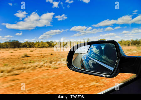 Australian Outback sol rouge et scarse gommiers sous ciel bleu avec vue arrière voiture conduite par miroir flou côté route. Banque D'Images