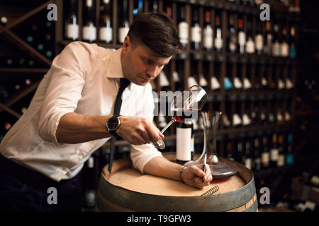 Super femme degustator contrôle du vin dans le bar à vin. Bouteille de vin différents dans l'arrière-plan de la photo. copy space Banque D'Images