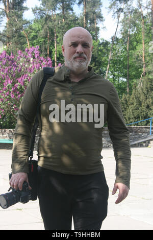 Homme barbu aux cheveux gris avec un appareil photo dans un parc fleuri Banque D'Images