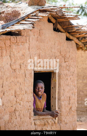 Malawian boy vu regardant par une fenêtre dans un mur de sa hutte de terre dans un village au centre du Malawi Banque D'Images