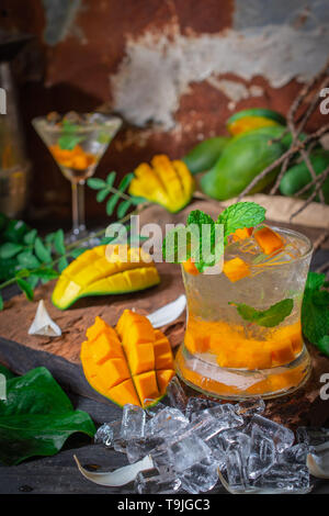 Mangue fraîche glace soda verre sur la table en bois de mangue, il y a des coupes de glace et de feuilles autour. Banque D'Images