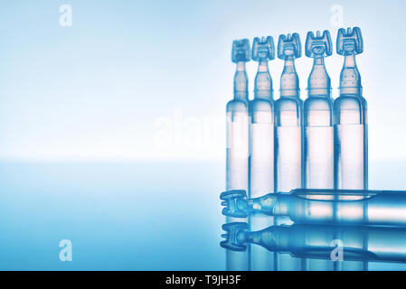 Des larmes artificielles gouttes pour les yeux encapsulés dans des pipettes en plastique et réfléchi sur une table en verre avec fond bleu. Composition horizontale. Vue avant Banque D'Images