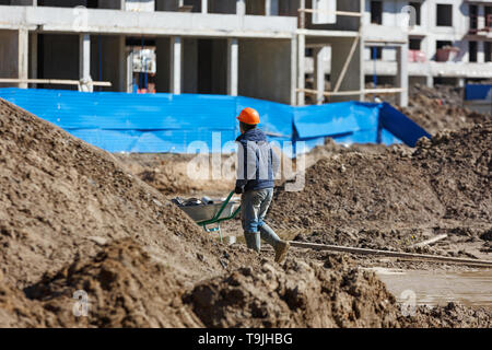 Un travailleur dans un casque porte une brouette dans le contexte des débris de construction. Banque D'Images