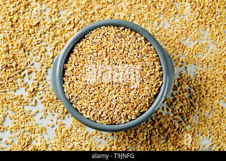 Portrait d'un bol en céramique gris avec des grains de blé tendre sur une table pleine de quelques grains de blé plus tendre Banque D'Images