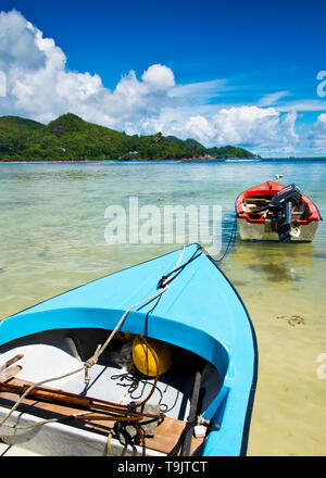 Petits bateaux de pêche colorés peints en bleu et rouge se sont rassemblés, avec ancrage de moteur extérieur dans la baie turquoise de l'océan, Seychelles, Banque D'Images