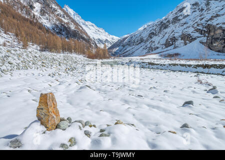 Cairn marque le sentier le long d'une rivière, ruisseau de montagne avec plein de l'eau glaciaire de montagnes à proximité. Neige fraîche couvrant le fond de la vallée. Banque D'Images