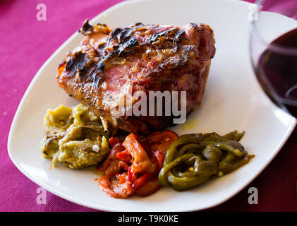 Jarret de porc grillé appétissant servi avec garniture de légumes et de vin rouge Banque D'Images