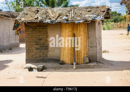 Une petite cabane de torchis avec un toit d'herbe et une porte faite d'un tapis de roseaux dans un village de Malawi Banque D'Images