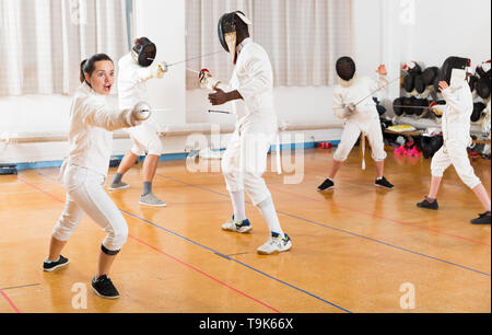 Portrait d'une jeune femme portant l'uniforme d'escrime fleuret en pratiquant avec salle de sport Banque D'Images