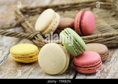 Colorful macarons français éparpillés autour sur la surface en bois et rotin Banque D'Images