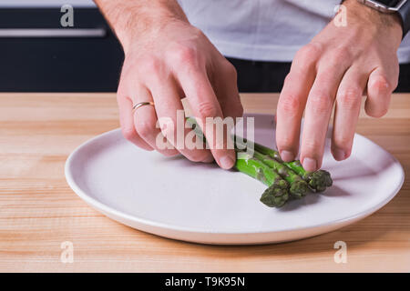 Gros plan des mains pose d'asperges vertes à la vapeur sur la plaque, préparer la présentation des aliments Banque D'Images