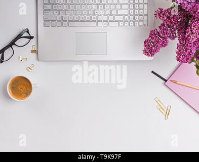Concept de poste de travail féminin moderne. Ordinateur portable, de café, de belles fleurs violettes et roses bloc-notes sur le tableau blanc, vue du dessus. Banque D'Images