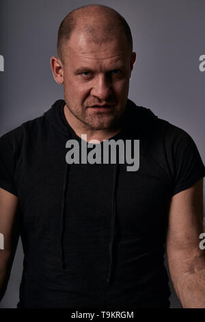 La criminalité en colère triste homme avec tête chauve à mystère et agressif en chemise noire sur fond gris foncé. Closeup portrait. Banque D'Images