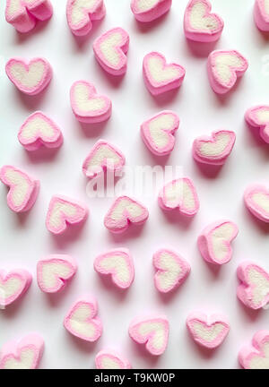 Vertical Image de rose pastel et blanc en forme de coeur bonbons guimauve éparpillés sur fond blanc Banque D'Images