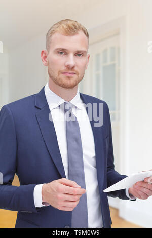 Friendly realtor mâle dans une veste et cravate bleu avec l'ordinateur tablette dans une salle vide d'un immeuble ancien rénové. Banque D'Images