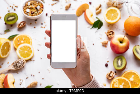 Female hands holding smartphone sur une alimentation saine, l'arrière-plan à l'aide femme recherche téléphone mobile apps avec un régime alimentaire plan de nutrition, Cuisine vegan granola aux fruits Banque D'Images