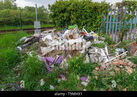 Un tas de détritus, gravats et déchets des sous-évaluées les décharges sauvages illégales à côté d'une ligne de chemin de fer à Nursling, Test Valley, Southampton, Hampshire, Royaume-Uni Banque D'Images