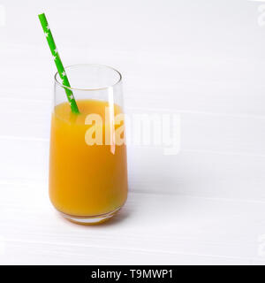 Grand Verre de délicieux jus d'orange fraîchement pressé avec paille verte sur le tableau blanc en bois debout. Banque D'Images