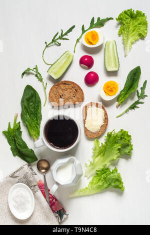 Petit déjeuner sain. Une tasse de café à moitié œufs durs, de pain grillé avec du beurre et de feuilles d'épinards et de salade sur un tableau blanc Banque D'Images