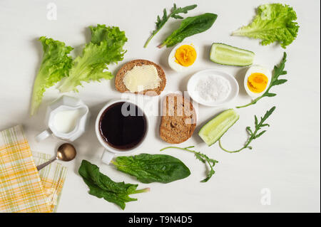 Petit déjeuner sain. Une tasse de café à moitié œufs durs, de pain grillé avec du beurre et de feuilles d'épinards et de salade sur un tableau blanc Banque D'Images