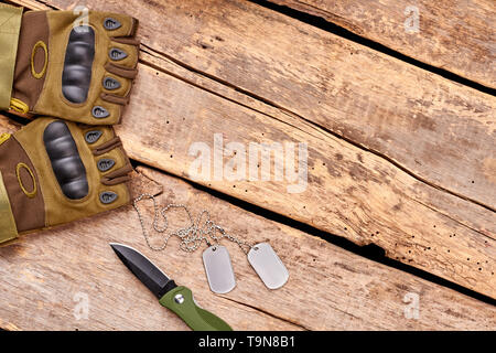 Gants militaires, couteau et dog tags sur bois avec copyspace. Banque D'Images