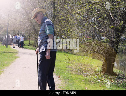 Un vieil homme marche à travers le parc et se tourne vers mon appareil photo. Banque D'Images