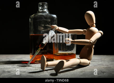 Petit mannequin en bois avec la seringue et de l'alcool sur le tableau gris. Concept de mauvaises habitudes Banque D'Images