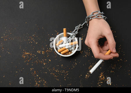 Les cigarettes à la chaîne pour main de femme sur fond sombre. Concept de toxicomanie Banque D'Images