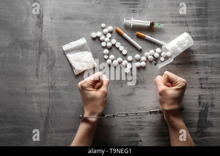 Femme junkie dans les menottes à l'aide de médicaments et de seringues sur fond gris. Concept de toxicomanie Banque D'Images