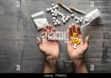 Femme junkie dans les menottes à l'aide de médicaments et de seringues sur fond gris. Concept de toxicomanie Banque D'Images