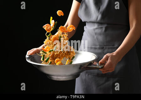 Woman cooking délicieux nouilles chinoises au wok sur fond sombre Banque D'Images