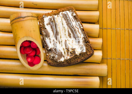 Sandwich avec pain de blé noir grossier et sweet curd et chocolat noir sur un stand de bambou et de bambou serviette avec perles de corail rouge. Il simple délicieux Banque D'Images