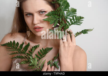 Portrait de belle femme avec des feuilles de fougère verte sur fond clair Banque D'Images