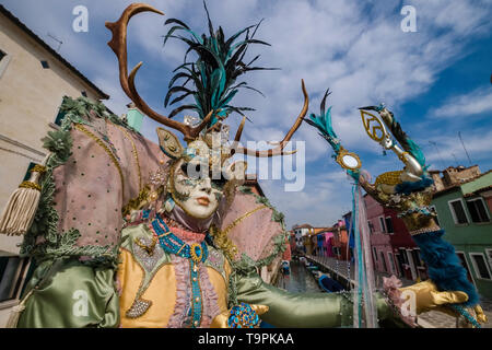 Une personne masquée feminin dans un beau costume créatif, posant sur l'île de Burano, célèbre le carnaval vénitien Banque D'Images