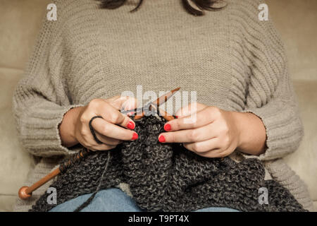 Girl with red nails le tricot de laine gris foncé avec des aiguilles en bois, assis sur une chaise, de l'artisanat avec de la laine Banque D'Images