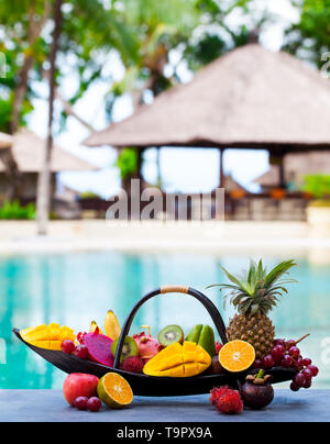 Assortiment de fruits tropicaux en bateau en bois. Piscine Tropicale arrière-plan. Copier l'espace. Banque D'Images