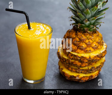 Avec de l'ananas, jus de fruits tropicaux sur smoothie pierre sombre arrière-plan. Close up. Banque D'Images