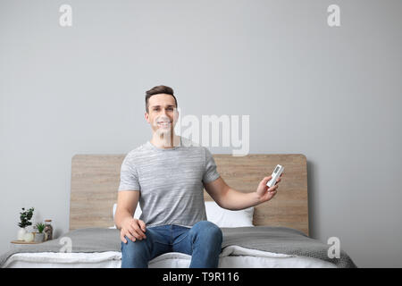 Jeune homme avec télécommande de climatiseur dans la chambre Banque D'Images