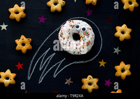 Météorite de beignets avec yeux couinent parmi les étoiles de cookies sur un tableau noir, drôle d'arrière-plan des animations pour les enfants avec de la nourriture, de l'espace concept Banque D'Images