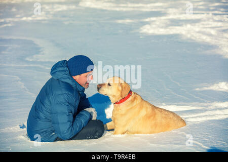 Un homme et un chien sont les meilleurs amis. L'homme avec le chien assis dans un champ neigeux en hiver Banque D'Images