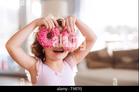 Une petite fille avec des beignets à la maison, avoir du plaisir. Banque D'Images